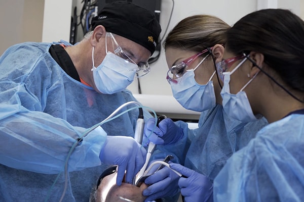 A dentist and two assistants working on a patient's mouth.
